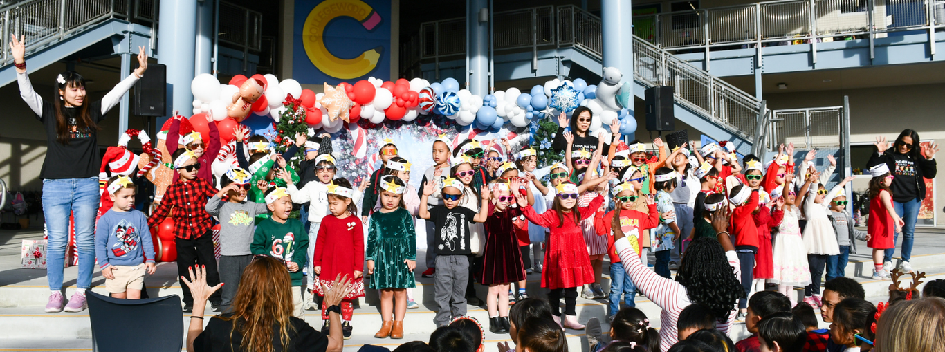 Children performing on stage wearing festive attire and hats, surrounded by decorations.