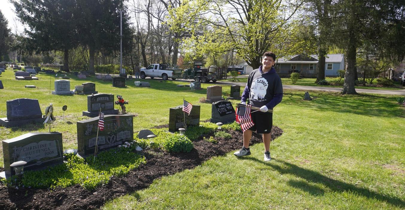 A student places American flags no gravesites of veterans as part of service day.