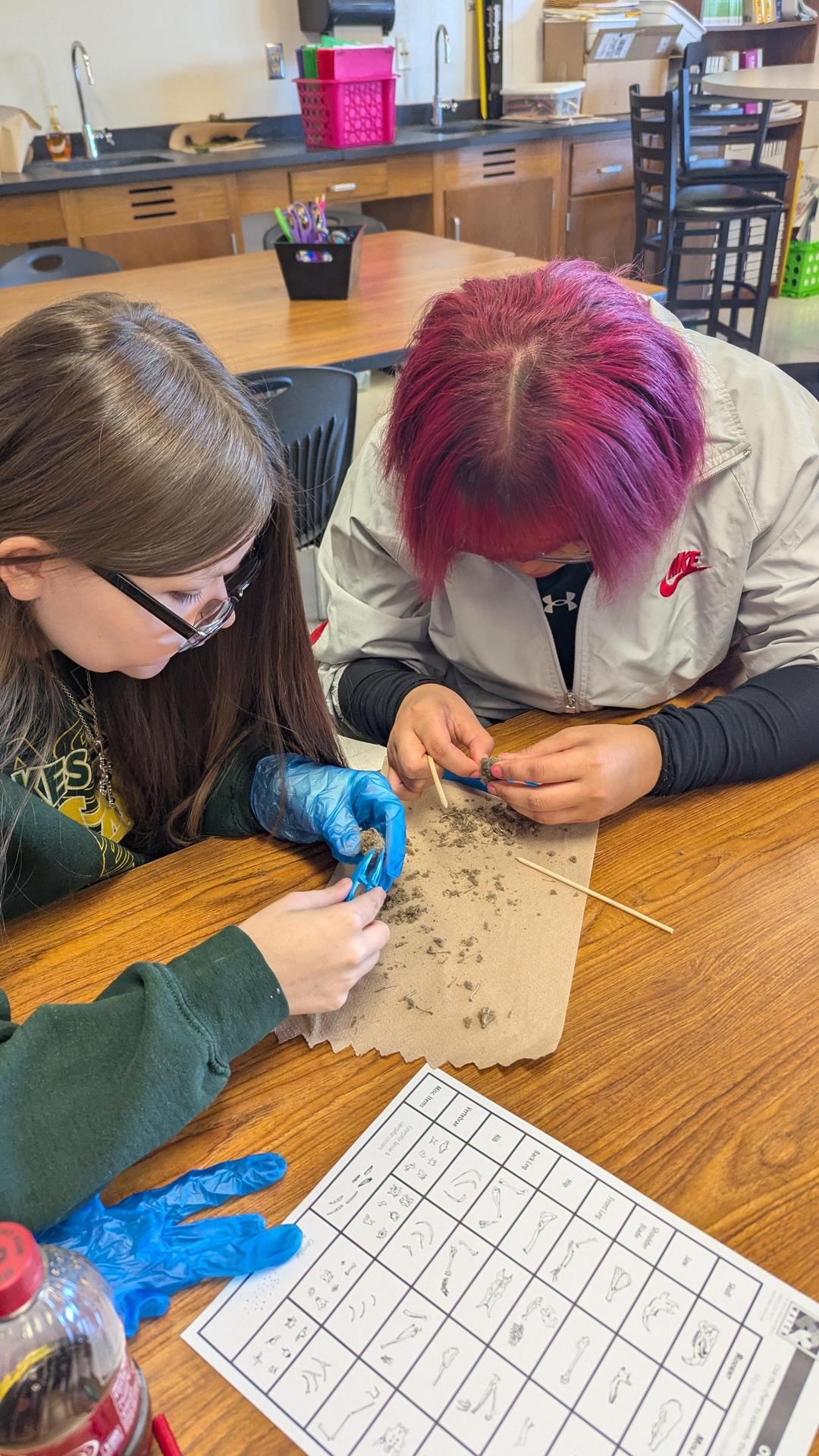 Two students examine materials on a table while working with clay.