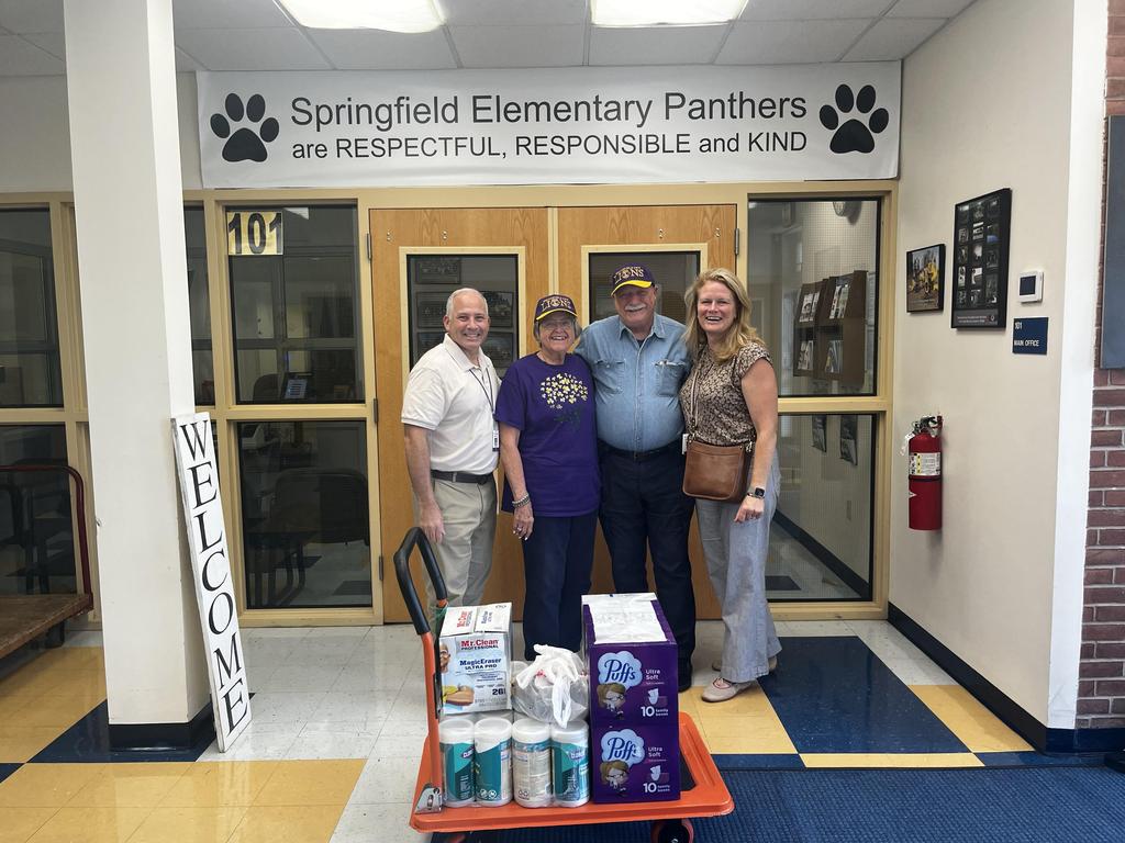 Group of four people in a school entrance with a cart of supplies.