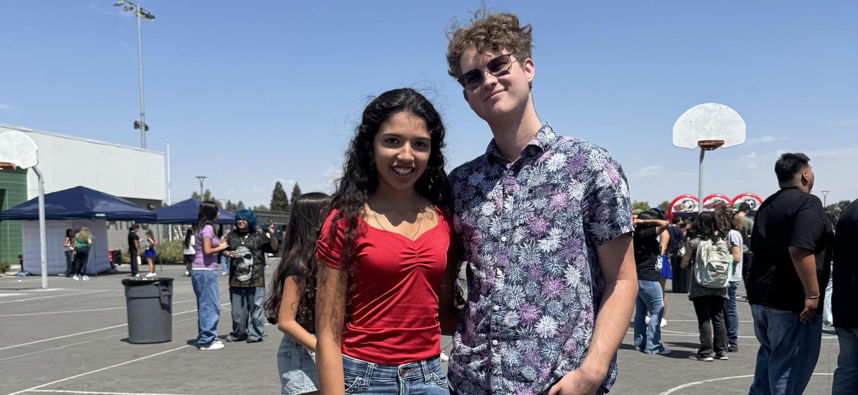 A couple poses for a photo at an outdoor gathering with others in the background.