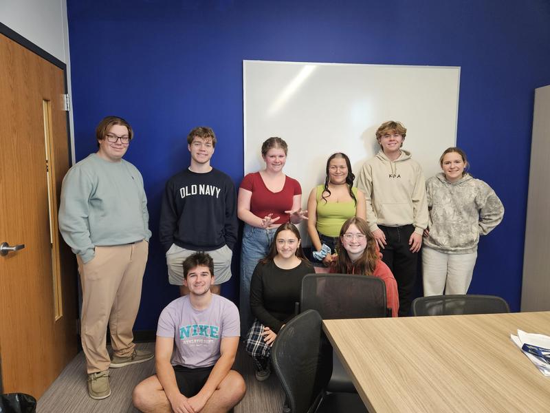 group of students that make up the trivia team leaning on blue wall