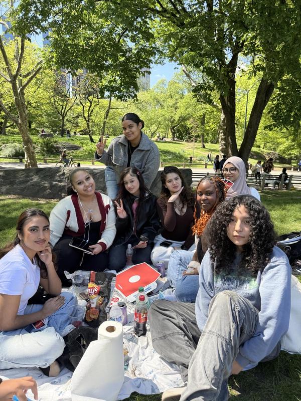 A group of eight people sitting together on a blanket in a lush green park.