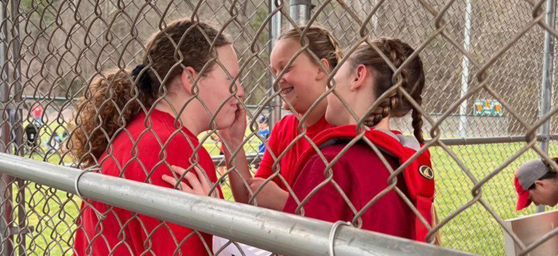 Three softball players stand in a dugout.