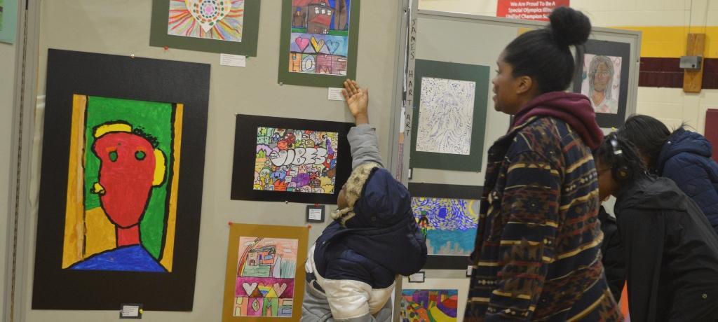 boy points out his artwork on display to a loved one
