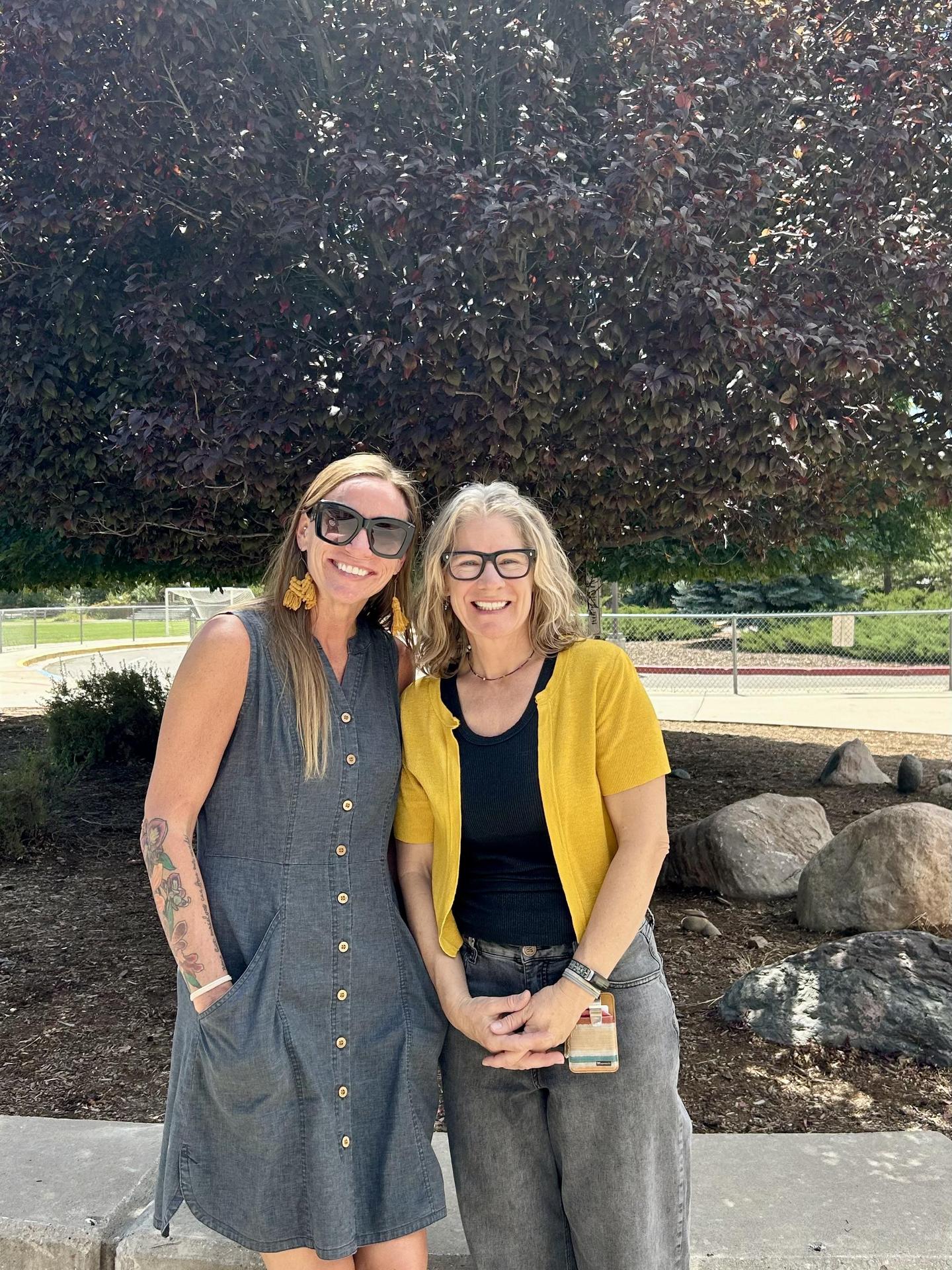 Two female teachers standing in front of a tree with red leaves
