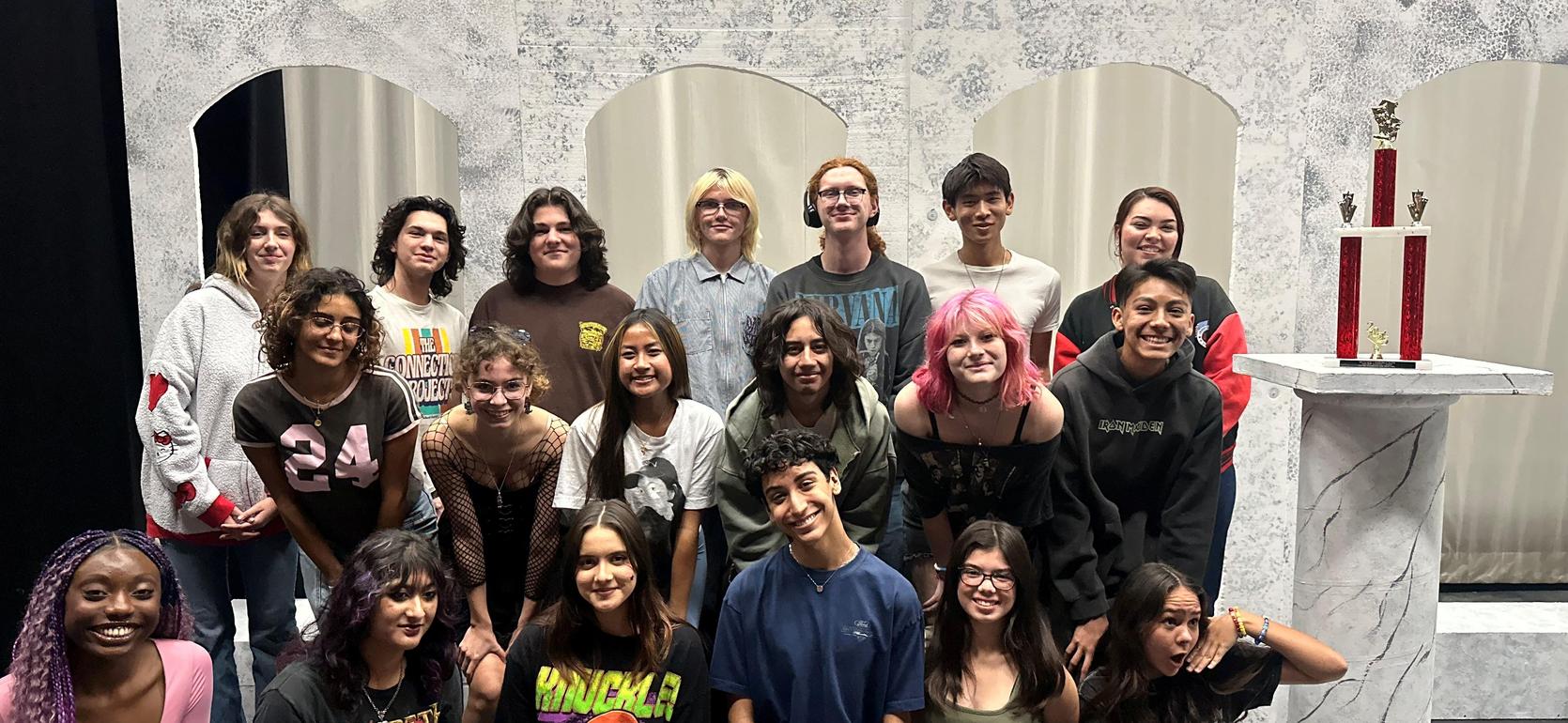 Group of students posing together in front of a trophy and decorated backdrop.