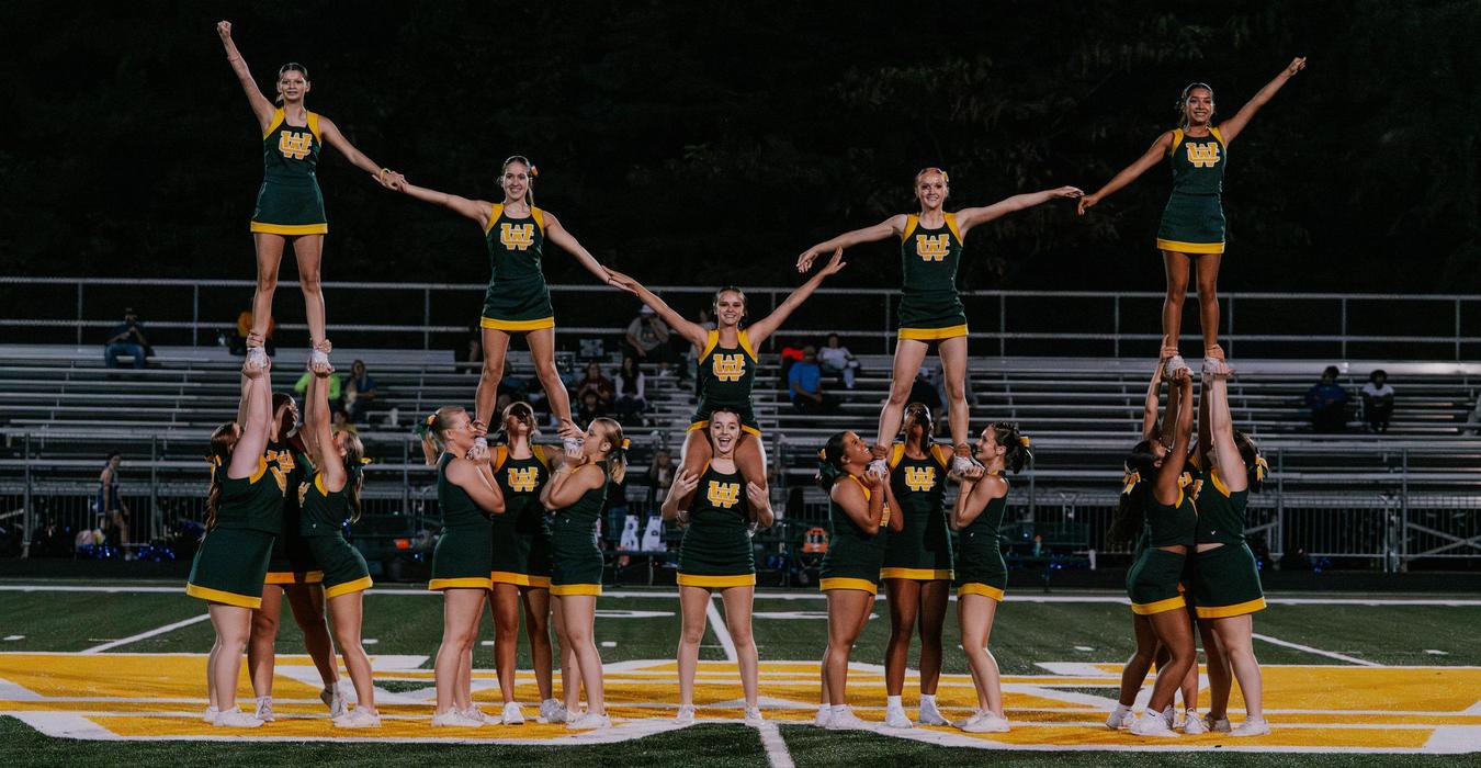 Cheerleading squad performing a pyramid stunt on a football field.
