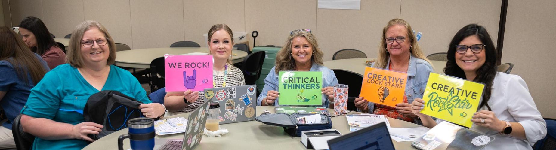 Group of five women holding signs that say, 'We Rock,' 'Critical Thinkers,' and 'Creative Rock Stars.'