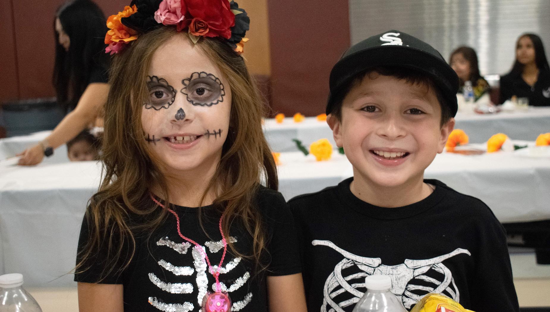 Two children smiling with face paint and costumes, seated at a table.