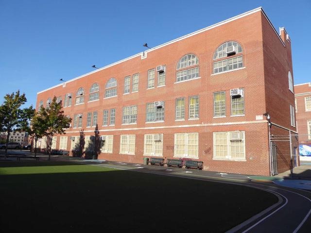 A brick school building with large windows and trees in the vicinity.
