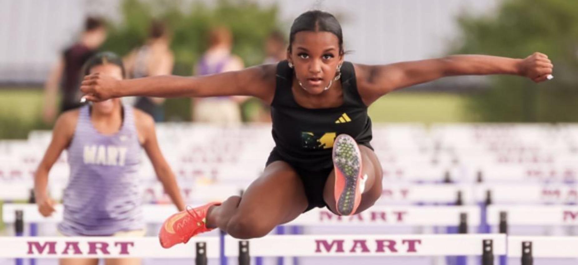 Girl track athlete jumping over a hurdle at Mart track meet