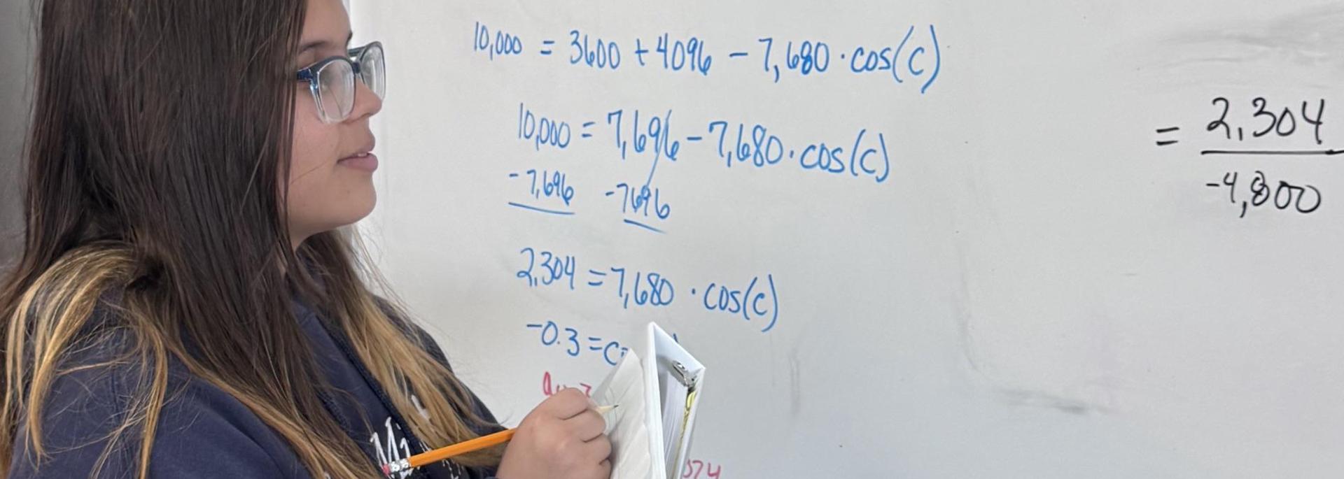 Student writing notes at a whiteboard filled with math equations.