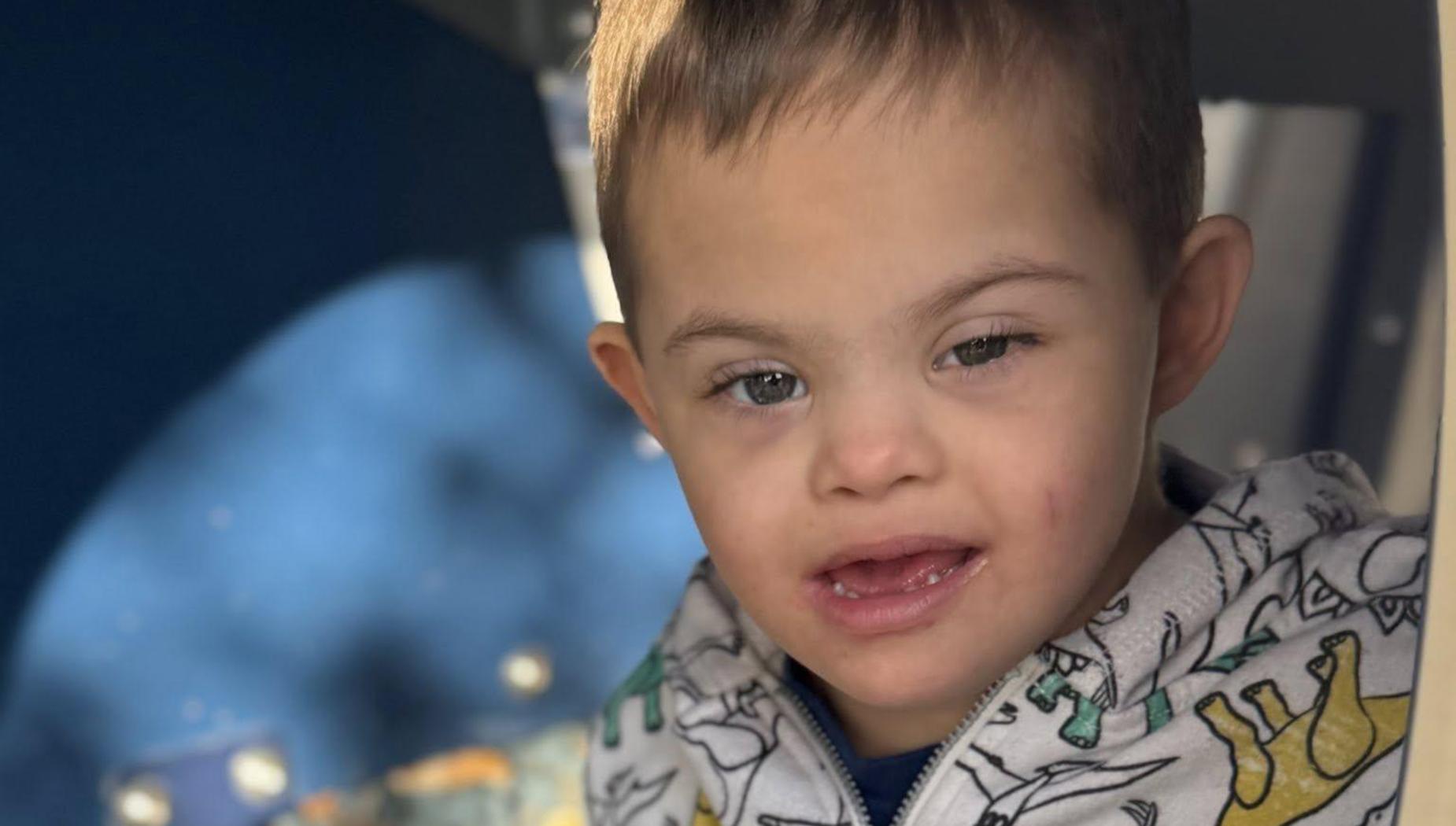 Close-up of a child in a dinosaur-patterned hoodie on playground equipment.