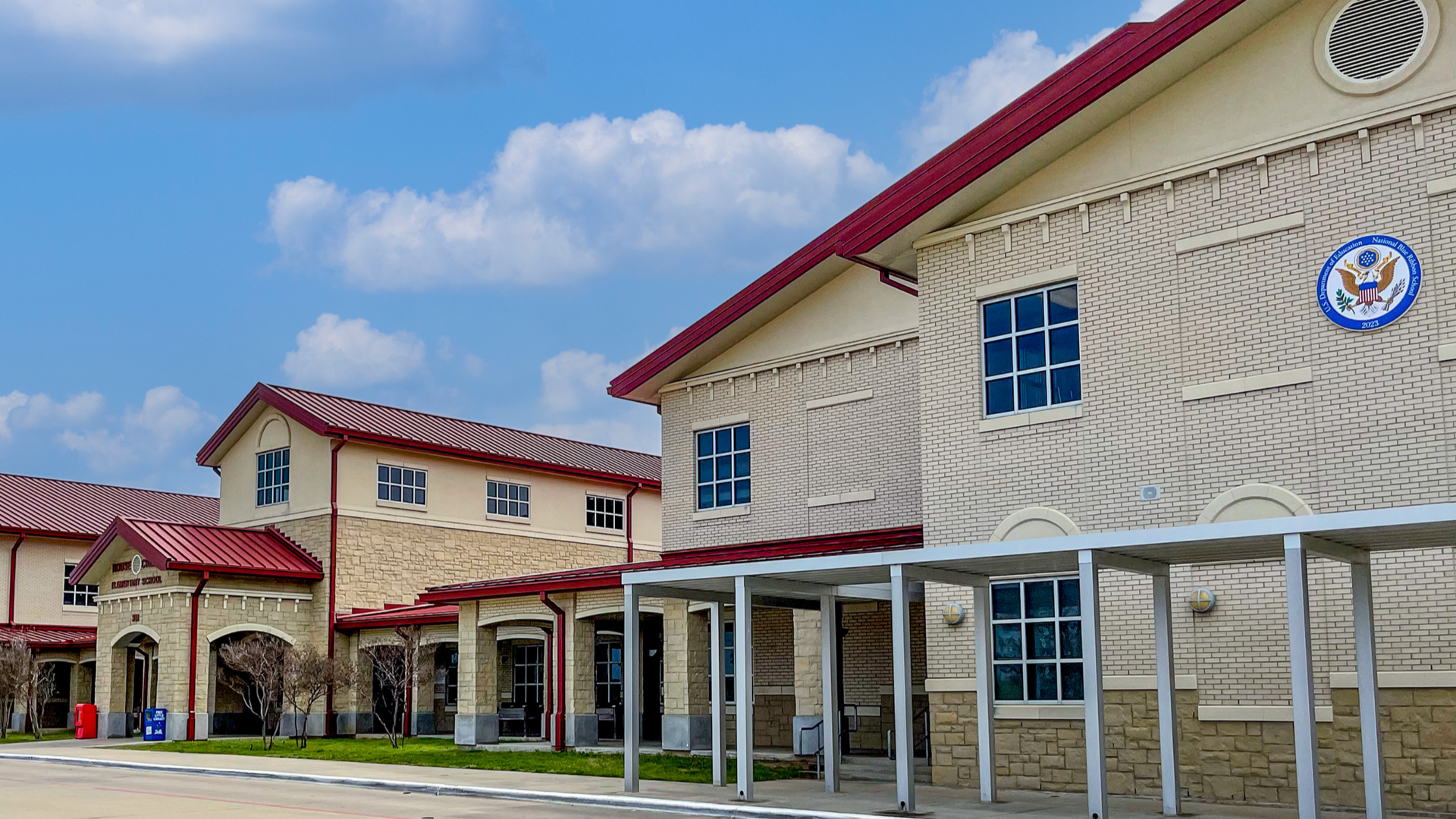Modern school building with red roofs under a cloudy blue sky.