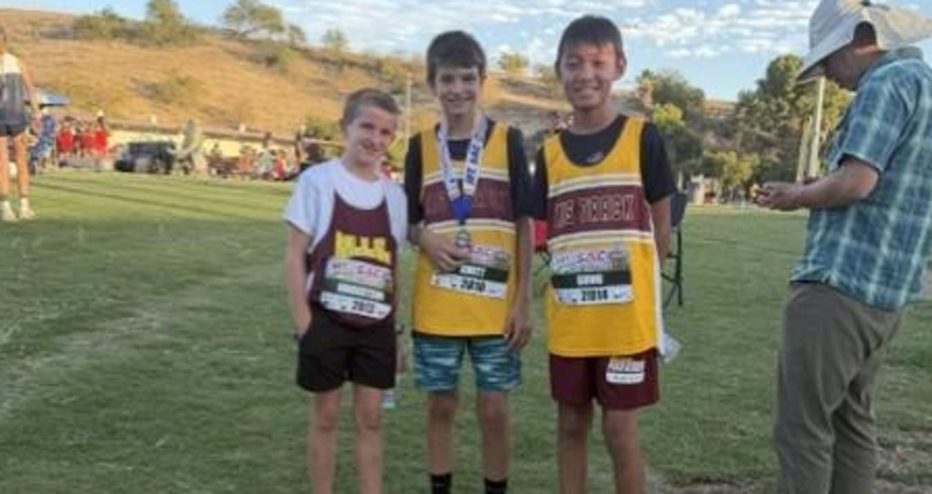 Three young athletes in racing jerseys standing on grass at an event.
