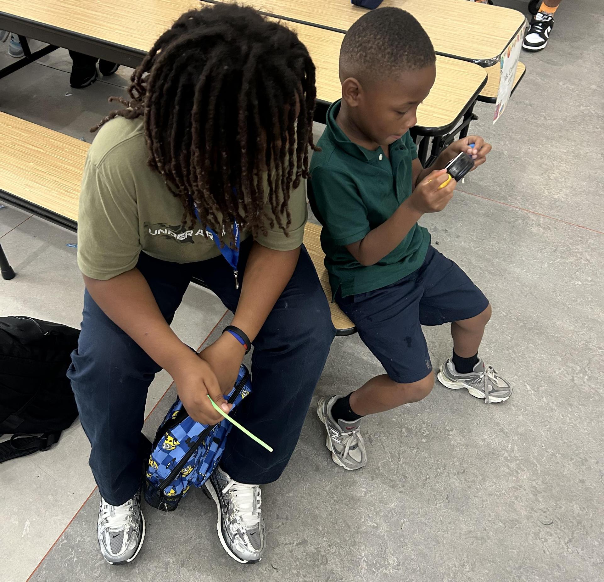 Two boys sitting on a bench, one with dreadlocks and the other holding a device.