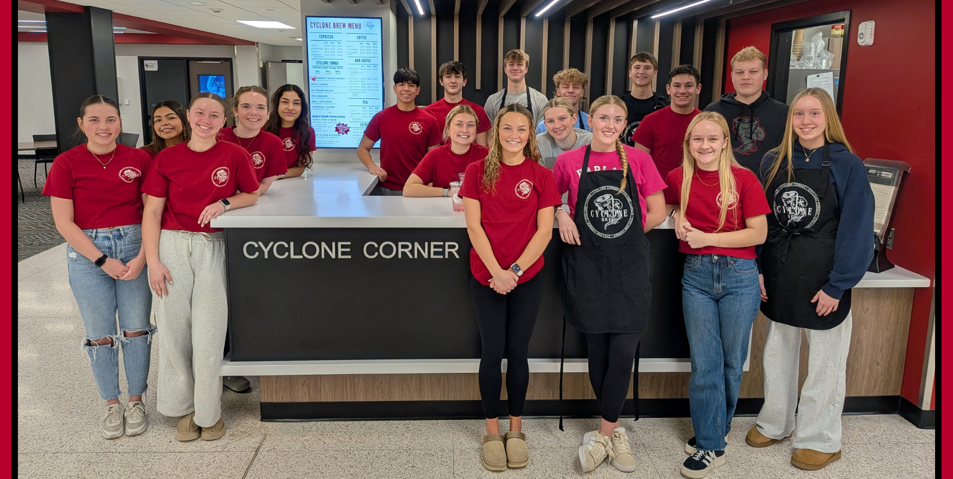 Group of students in matching shirts posing at a caf&eacute; counter.
