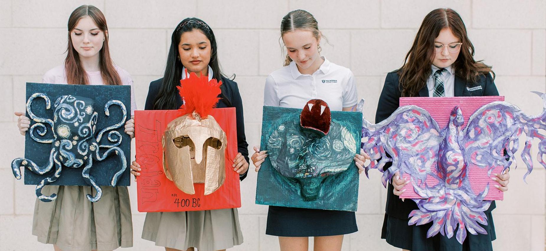 Four students hold up their artwork