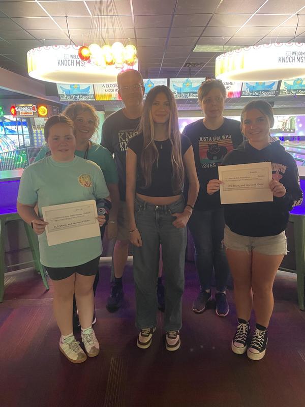 three students and three teachers in bowling alley holding checks for donation