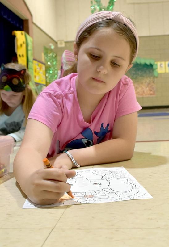 A girl coloring a drawing while wearing a pink shirt.
