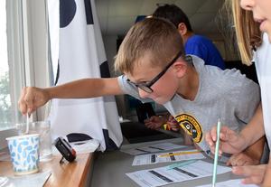 A boy stirring a cup of liquid while focused on an activity with peers.