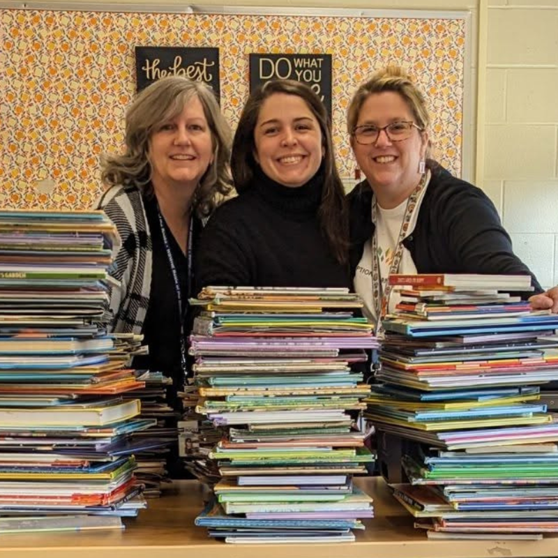 3 women behind stack of books