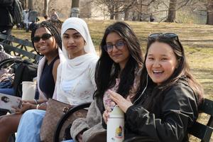 Four women sitting on a bench in a park, smiling and enjoying their time together.
