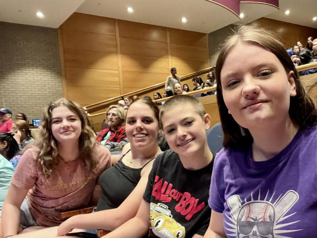 Four honor students smiling into the camera in an auditorium on a field trip.