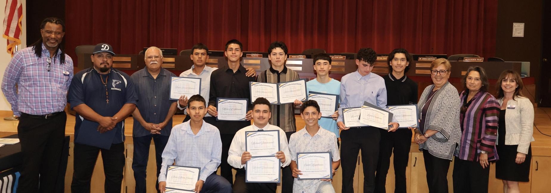 A group of students holding certificates, posing for a photo with adults in a school setting.