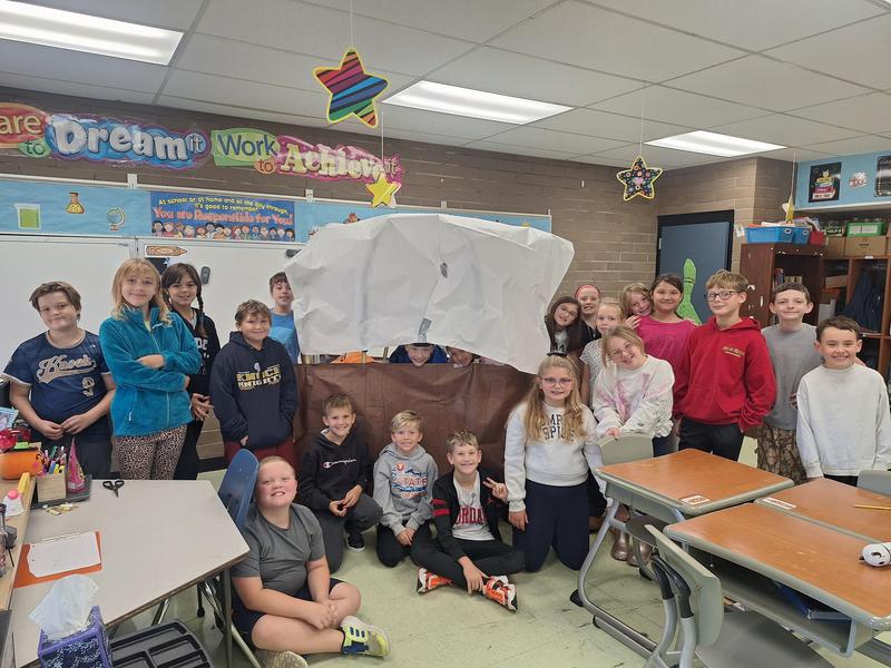 students sit in front of homemade conestoga wagon