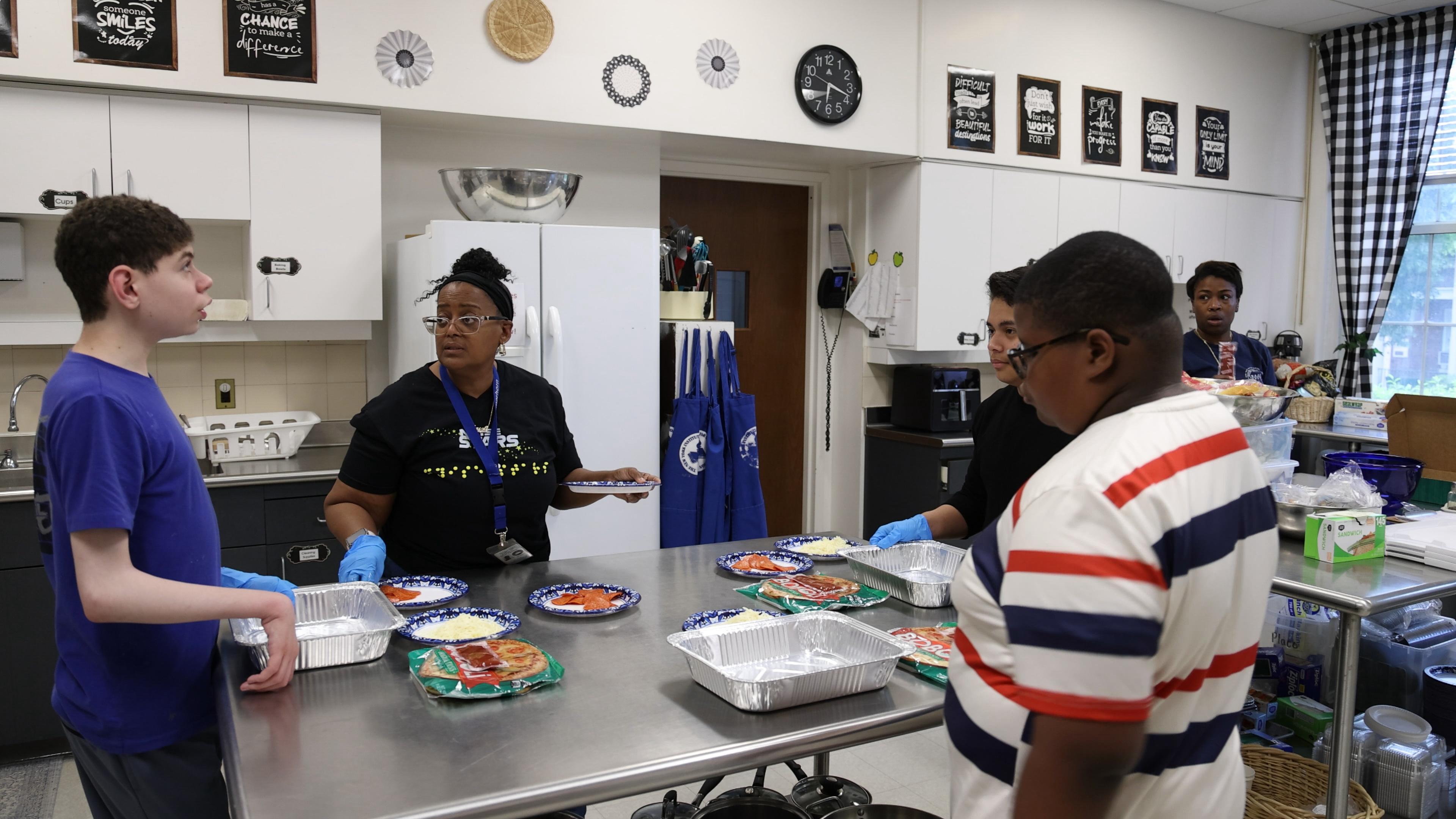 children and teachers stand in a kitchen, cooking