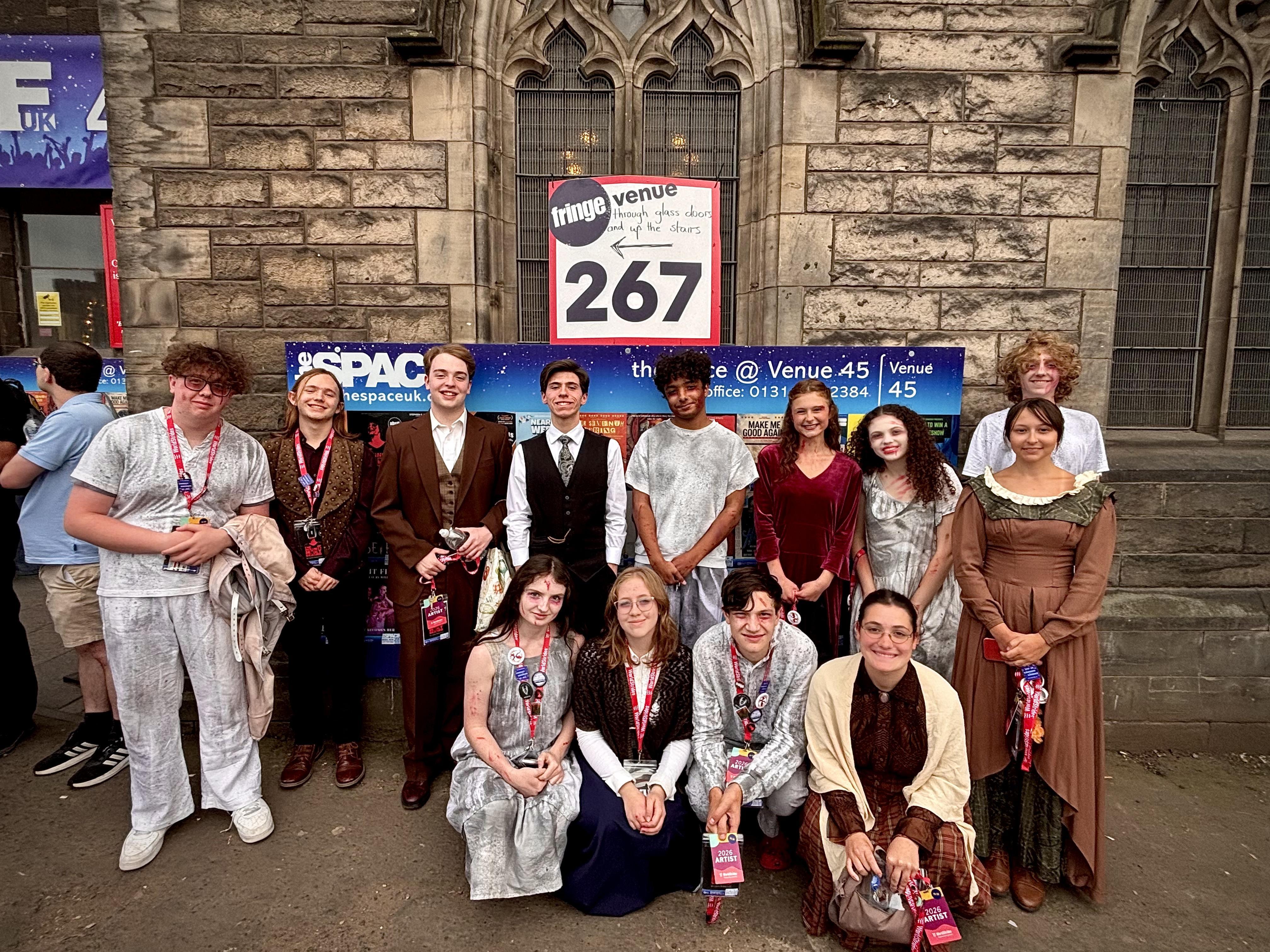 group of students in theatrical costume in front of sign reading space 267