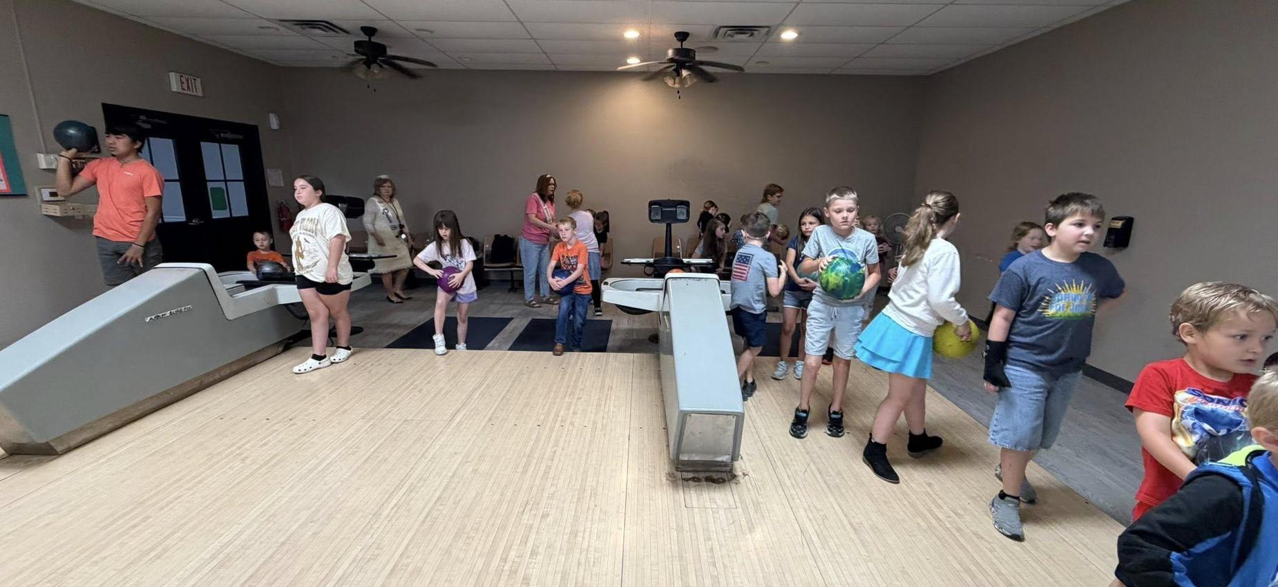 A lively bowling alley with many children carrying bowling balls and interacting.