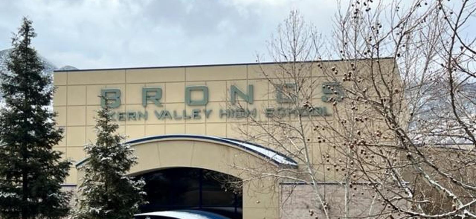 Bronze sign of Western Valley High School surrounded by trees under a cloudy sky.