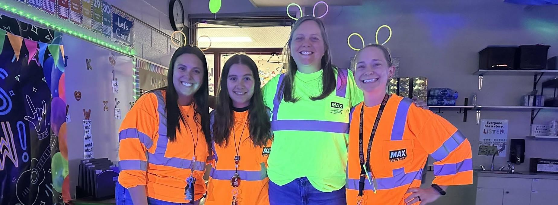 Four individuals wearing bright safety vests pose together in a brightly lit room.