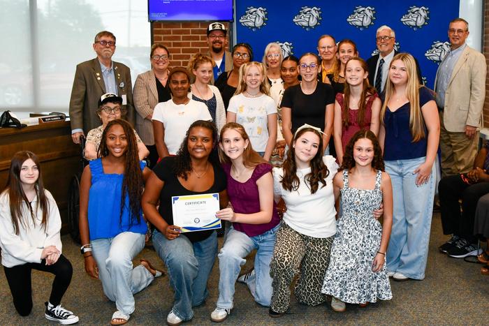 A group of girls with school board members, smiling and holding an award