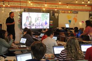 teacher stands in front of board with officials on screen