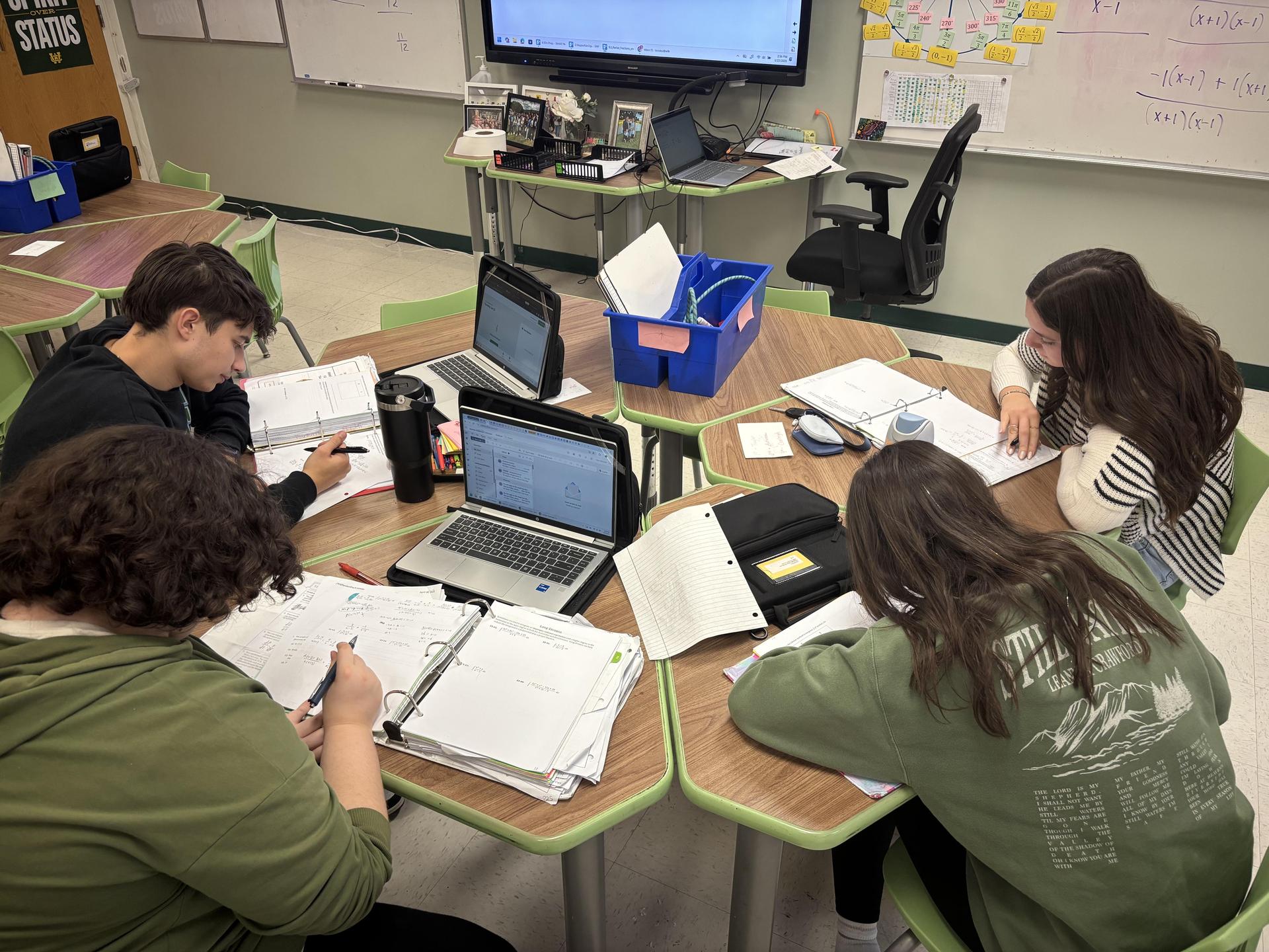 Four students focused on their work at a table, surrounded by laptops and notebooks.