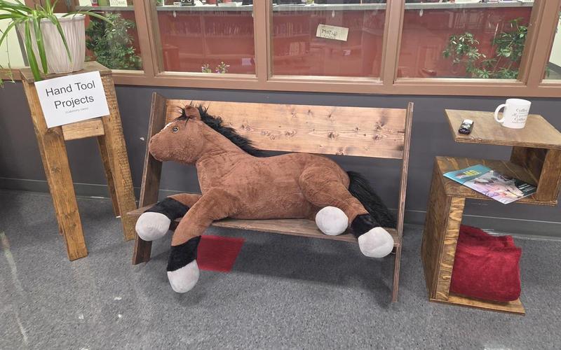 A stuffed horse lies on a wooden bench near project displays.
