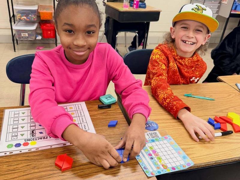Two children smiling while playing with colorful counting blocks in a classroom.