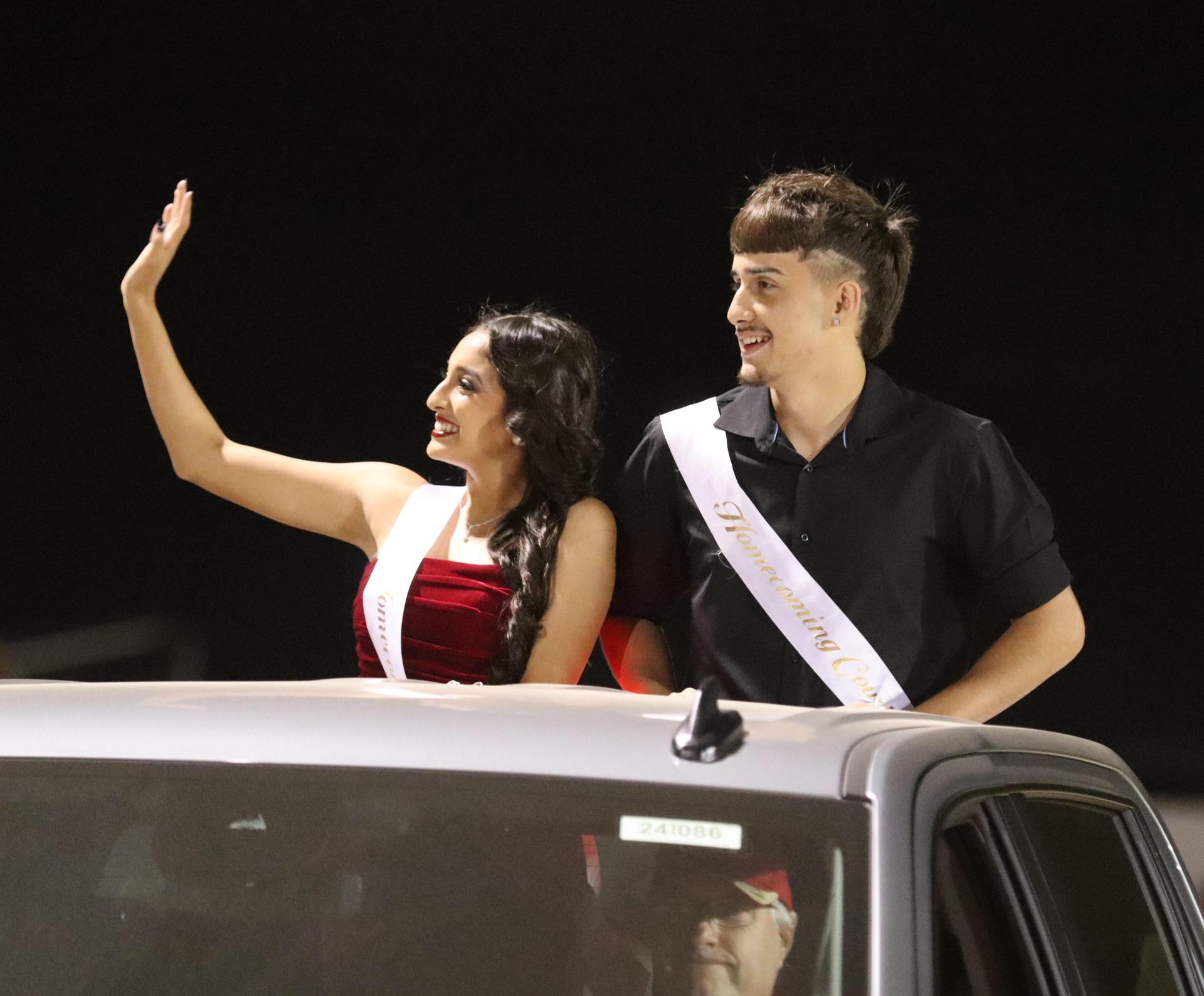 homecoming king and queen candidates entering the stadium in trucks