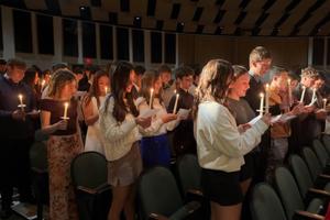 a large group of students holds candles for a ceremony in an auditorium