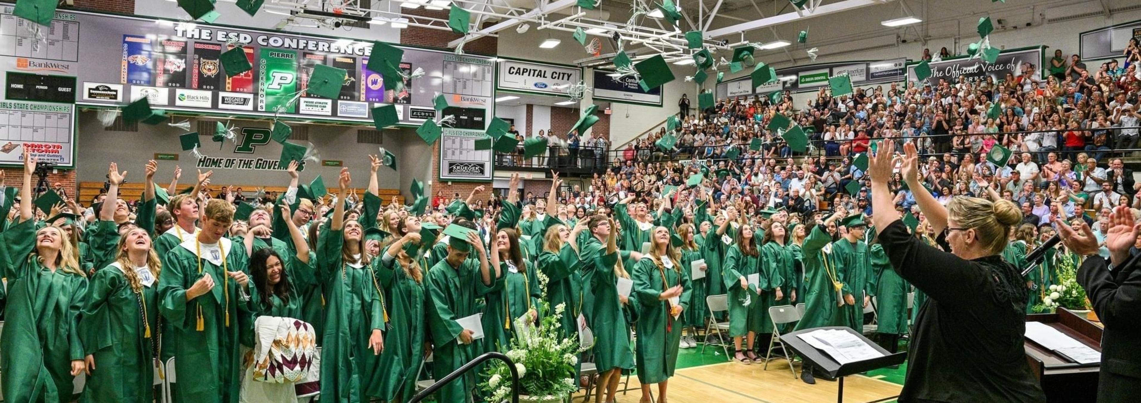 Graduates in green caps and gowns celebrate at a graduation ceremony.