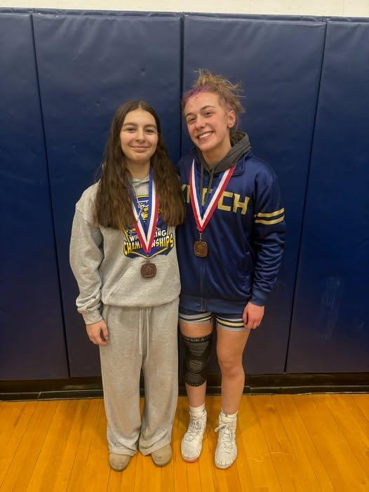 two girl wrestlers leaning on mat with medals around their necks