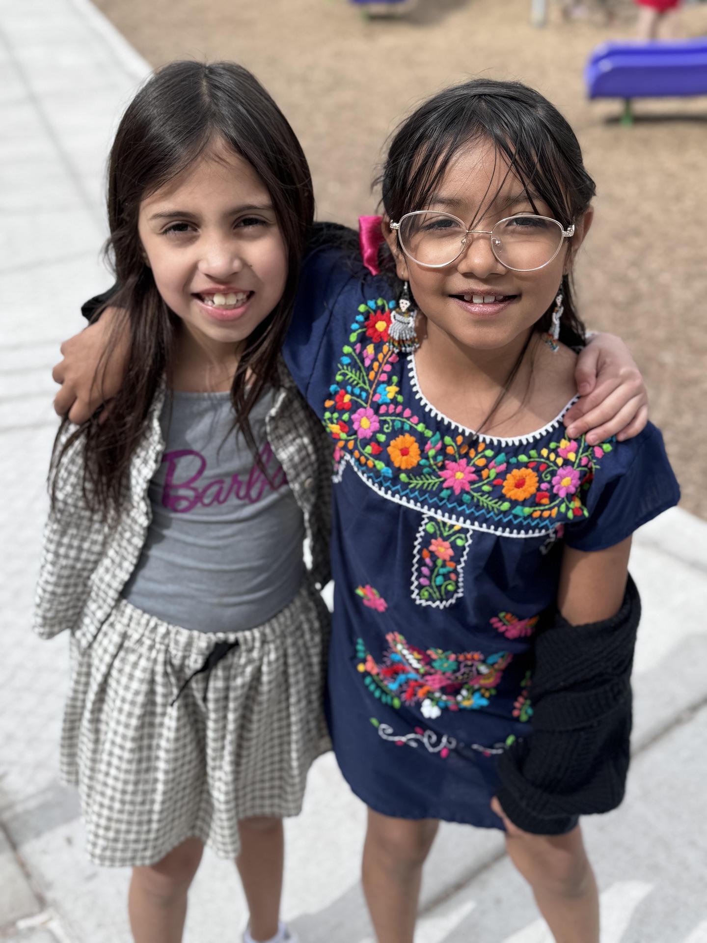 two students smiling with arms around each other on playground wearing colorful outfits