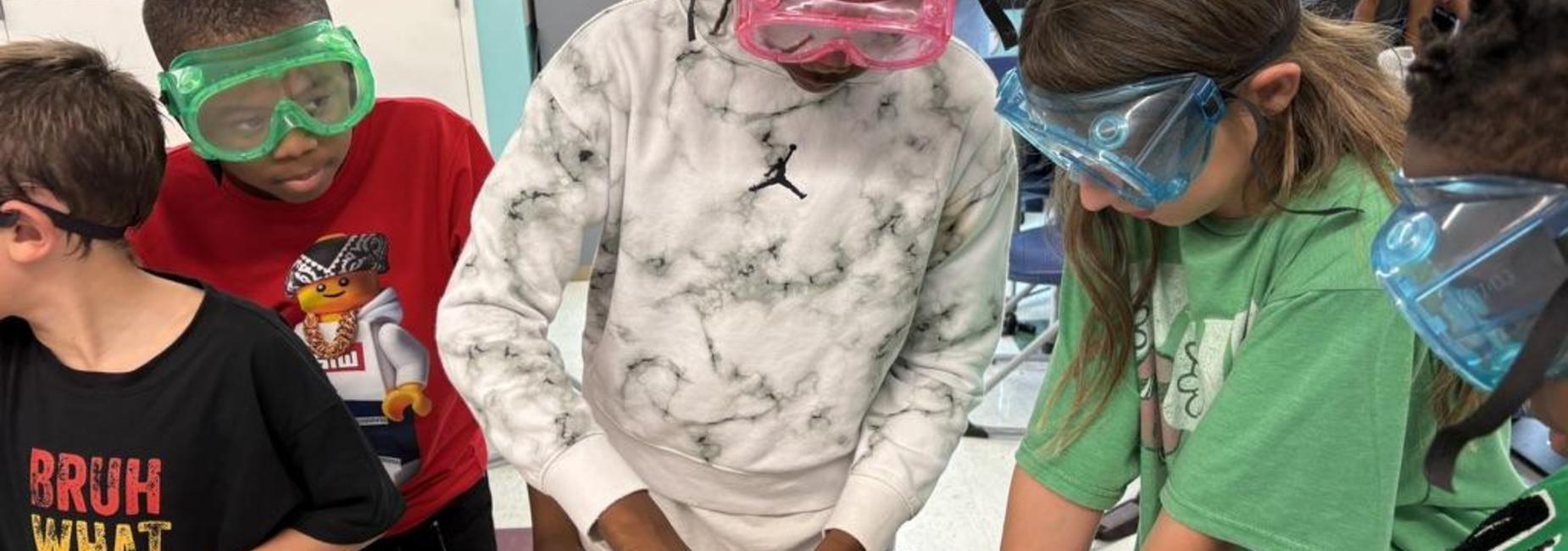 A group of children wearing safety goggles engaged in a hands-on science activity.