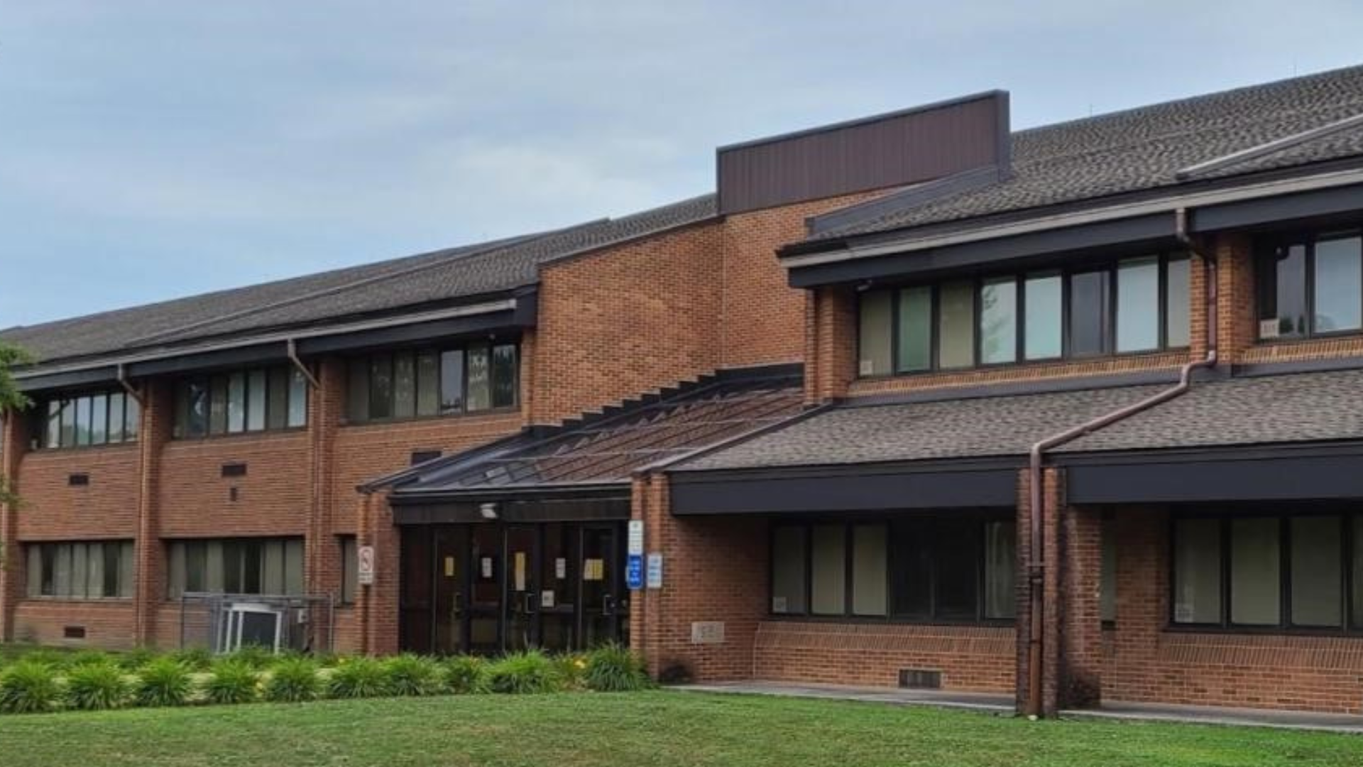 Brick building with large windows and a landscaped entrance.
