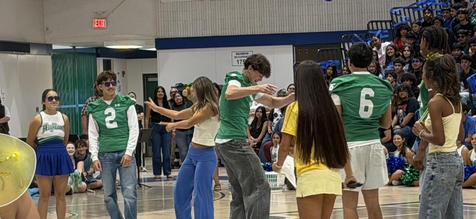 Students in green shirts perform on stage for an audience at a school assembly.