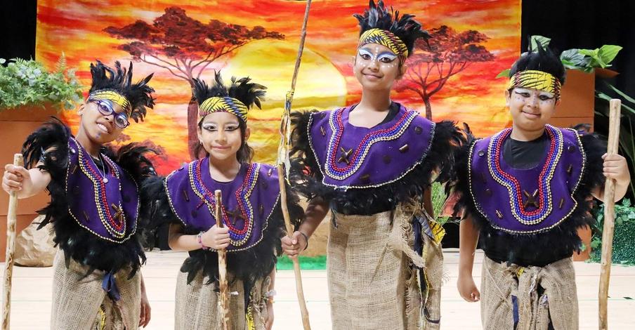 Four children in vibrant traditional costumes with sticks posing on stage.